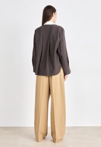 Brown plaid long-sleeve shirt with a white collar, paired with light beige wide-leg trousers. Both garments feature a relaxed fit.