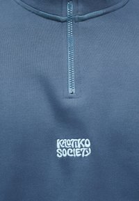 Μπλε φούτερ με μπλε ανοιχτό φερμουάρ μπροστά και λευκό κεντημένο κείμενο «KROTIKO SOCIETY» κάτω από το φερμουάρ.