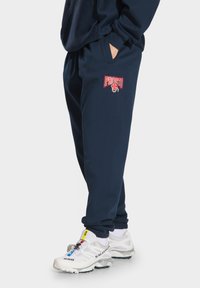 Granatowe dresy z miękkiego materiału, z elastycznym paskiem; na udzie znajduje się czerwone logo "PRESTO". Noszone z białymi sneakersami.