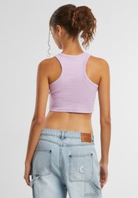 Lys lilla avkortet tanktop med ribbestruktur og racerback-design, sammen med lyseblå denimbukser med baklommer og logo detaljer.
