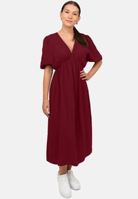 Bordeaux midi-jurk van een textuurstof met pofmouwen en een diepe V-hals, gecombineerd met witte sneakers voor een casual look.