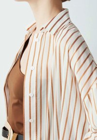 Striped button-up shirt in cream and rust, featuring a collar, vertical lines, and lightweight fabric. Includes white buttons and relaxed fit.