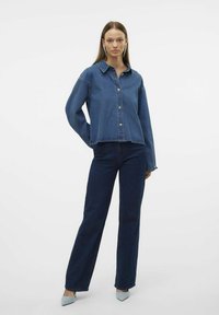 Jeans jakna v srednji modri barvi s ovratnikom in sprednjimi gumbi, kombinirana s straight-leg temno modrimi kavbojkami. Strukturirana tkanina, sproščen dizajn.