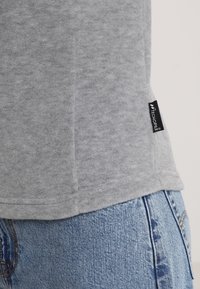 Szara, polarowa koszulka z krótkim rękawem o zaokrąglonym dole i metce bocznej z napisem "TECNOPILE". Miękka w dotyku, dopasowana. Dżinsy widoczne poniżej.