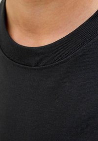 Fekete pamut crewneck gallér, ribbelt szerkezetű és sima anyagú, közelről bemutatva a nyakkivágást és a környező bőrt.