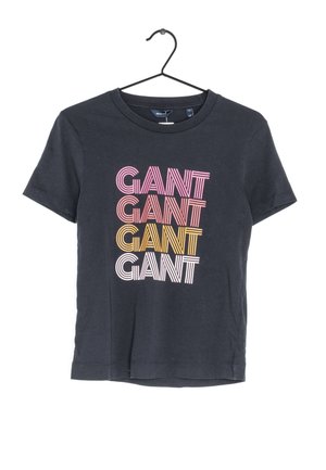 Camiseta negra de manga corta en una percha con la palabra "GANT" repetida cuatro veces en texto a rayas de colores rosa, melocotón, amarillo y blanco en el frente.