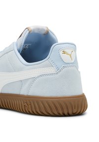 Zapatilla de ante azul claro con acentos blancos, suela de goma, collar acolchado y detalle del logo dorado en el talón. Vista lateral de la parte trasera.