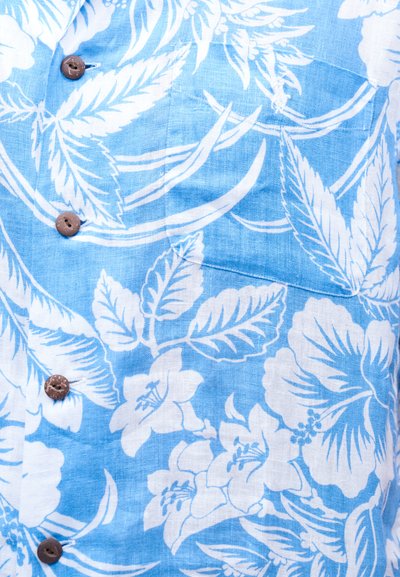 Világoskék szövet fehér trópusi virág- és levélmintákkal, középen barna gombokkal díszítve.