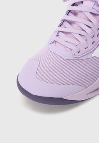 Šviesiai violetiniai sportiniai batai su tekstūruotu tinkleliu, plokščiomis raištelėmis ir kontrastinga tamsesnio violetinio guminio padu. Turintys šiuolaikišką, modernų dizainą.