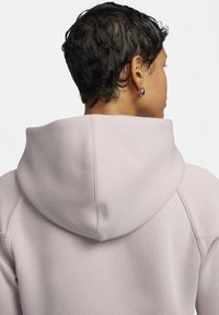 Lichtroze hoodie met een zachte textuur, voorzien van een grote capuchon en stikdetails aan de achterkant. Geen vooraanzicht zichtbaar.