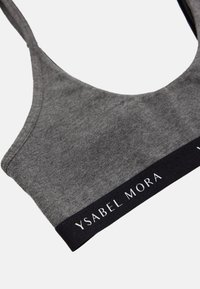 Sostén gris hecho de material suave con escote redondeado y una banda elástica negra que presenta "YSABEL MORA" en texto blanco.