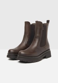 Bottines en cuir brun avec des panneaux élastiques sur les côtés, semelles en caoutchouc épaisses et détails de couture. Comprend des tirettes pour un enfilage facile.