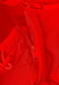 Röd vadderad tyg med slät textur, med dragkedjestängning och dragsko detaljer. Dragkedjans dragare har en logotypprägling.