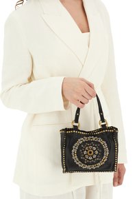 Borsa in pelle nera con embellishments metallici circolari, borchie dorate e doppi manici. Superficie testurizzata e dettagli decorativi.