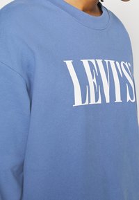 Sudadera azul de algodón, con un gran logo blanco de "LEVI'S". La tela es suave y tiene un diseño de cuello redondo.