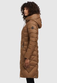 Hnědý prošívaný dlouhý kabát s kapucí, se černými kovovými detaily a bočním zipem, texturovaný materiál a přiléhavý silueta.