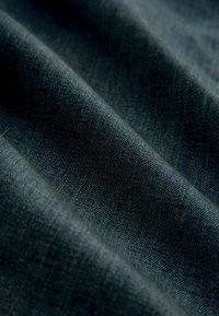 Țesătură împletită de culoare bleu închis, expusă cu o textură vizibilă și o ușoară strălucire, având pliuri diagonale care ilustrează adâncime și mișcare.