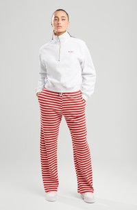 Gray zip-up sweatshirt with a high collar and red text; red and white striped wide-leg pants with a drawstring waist, paired with white shoes.