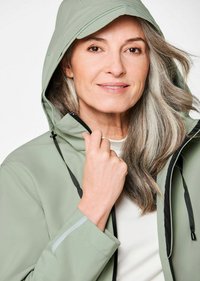 Lichtgroene waterdichte jas met capuchon, zwarte accenten en verstelbare trekkoorden, met een ritsluiting en reflecterende details.
