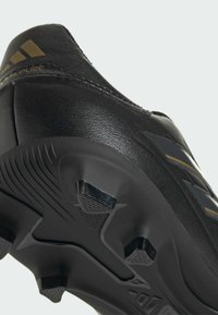 Zapato deportivo de cuero negro con suela texturizada. Presenta un diseño elegante, detalles metálicos y tachuelas colocadas estratégicamente para mejorar la tracción.