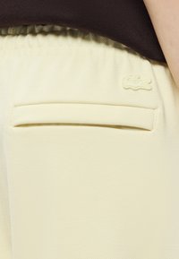 Ανοιχτόκίτρινα σορτς κατασκευασμένα από υφασμάτινο ύφασμα, με πίσω τσέπη και διακριτικό κεντημένο λογότυπο πάνω �από αυτήν. Ορατή ελαστική μέση.