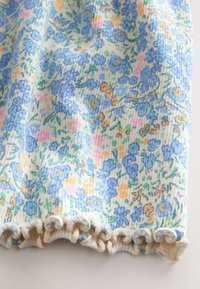 Blommigt tyg med blå och gula blommor på en ljus bakgrund. Texturerat ribbat mönster med en volangkant.