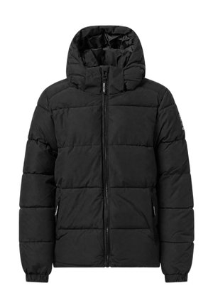 Garçon portant une doudoune noire, un sweat à capuche zippé noir, un jean bleu et des baskets vertes, debout les mains dans les poches.