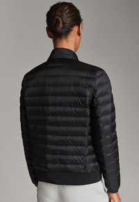 Doudoune noire au design ajusté, avec un motif matelassé horizontal et des poignets côtelés. Son style minimaliste se caractérise par un col montant.