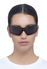 Czarne prostokątne okulary przeciwsłoneczne z ciemnymi soczewkami, charakteryzujące się eleganckim designem oprawy oraz małymi metalowymi akcentami przy zawiasach.