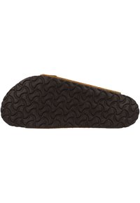 Bruine suède slipper met een gestructureerde zwarte rubberen zool met een golvend patroon, ontworpen voor comfort en binnengebruik.