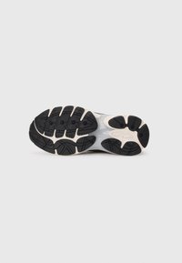 Black rubber sole with deep treads, featuring a gray midsole and cream accents. Designed for traction and flexibility.
