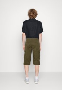 Chemise en lin noir à manches courtes associée à un short cargo vert olive. Baskets visibles en bas, avec des accents blancs et gris.