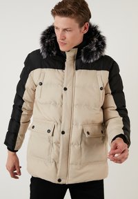 Giubbotto imbottito beige e nero con collo in pelliccia sintetica, dotato di chiusura con zip e bottone, due tasche frontali e polsini a costine.