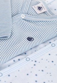 Lichtblauwe katoenen overhemden gestapeld. Eén heeft horizontale strepen, de ander heeft een sterrenpatroon. Beiden hebben knopen en een logo.