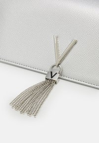 Silver-textured handbag featuring a V-shaped zipper pull and a chain tassel detail, with a smooth metallic finish.