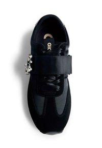 Sneaker nera con lacci in satin, una fascia larga sopra e una fibbia decorativa con gioiello sulla fascia, vista dall'alto.