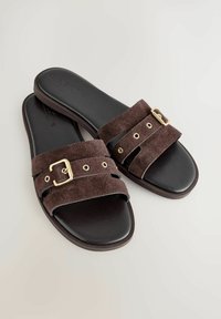 Sandales en daim marron avec deux larges brides, dotées de détails en métal doré et de découpes, sur une semelle intérieure noire rembourrée.