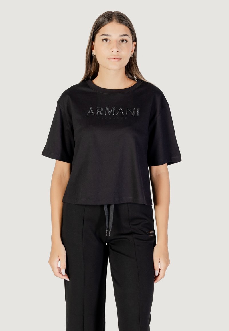 Camiseta negra corta de algodón, con un logo brillante de "ARMANI EXCHANGE" en la parte delantera, combinada con pantalones negros con cordón.