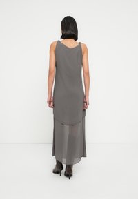  Μακρύ γκρι φόρεμα με ροή σχεδίου, που διαθέτει στρογγυλεμένο τελείωμα και δεμένους ιμάντες στον ώμο, κατασκευασμένο από ελαφρύ ύφασμα.