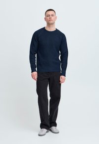 Navy knitted sweater with ribbed texture, rounded neckline, and long sleeves, paired with black straight-leg pants and grey sneakers.