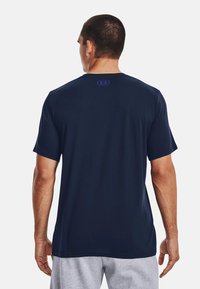 Marineblå kortermet T-skjorte med en jevn tekstur og rund hals. Har en lilla logo på baksiden.
