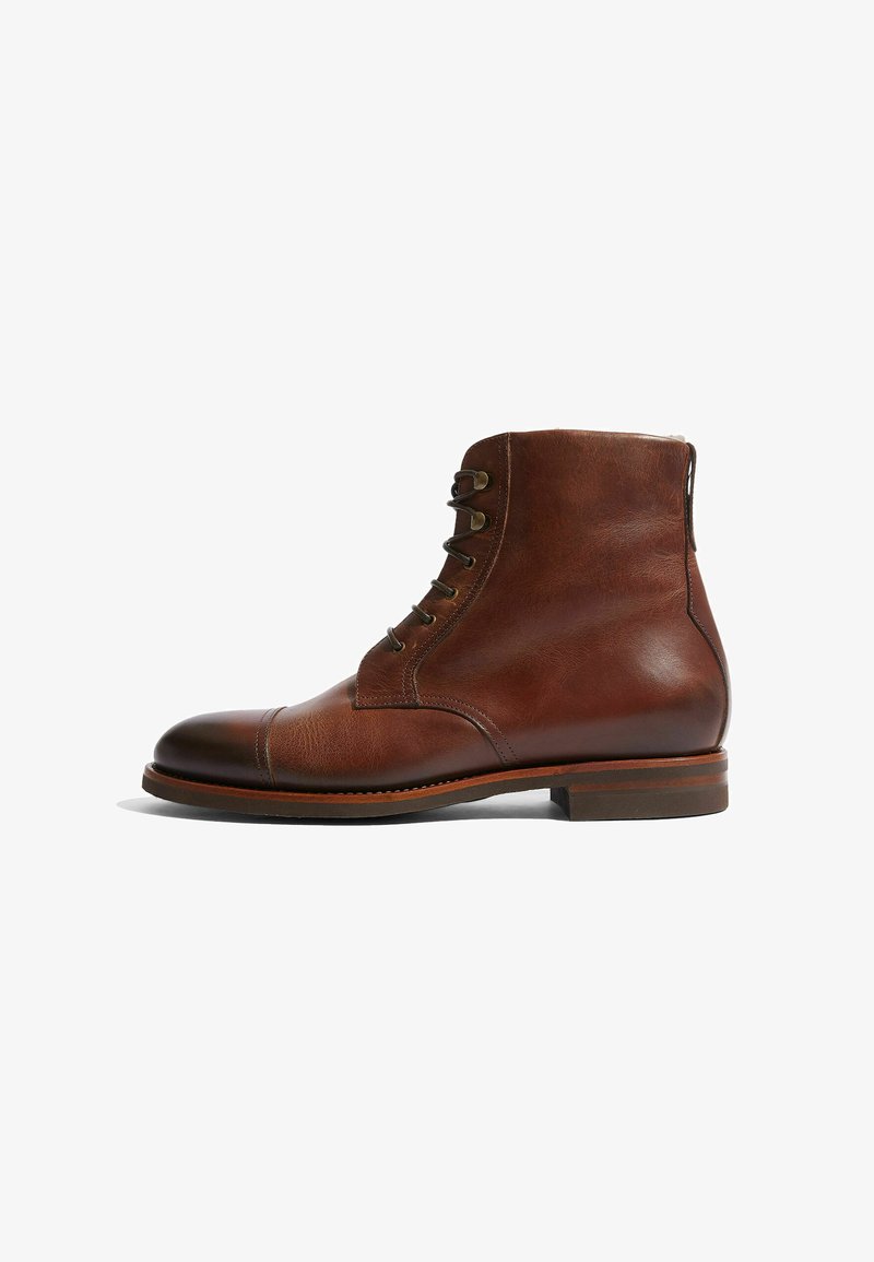 Stivali ankle in pelle marrone con punta arrotondata, 6 occhielli e un finish a superficie liscia. Presentano un tacco basso in legno e cuciture a contrasto.
