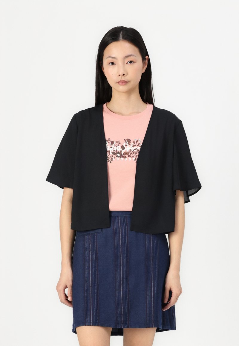 Svart kortärmad cardigan över en rosa t-shirt med blommönster, tillsammans med en blå jeanskjol med vertikala ränder.