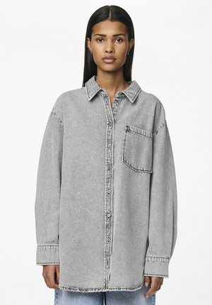 Camicia in denim grigio con colletto, maniche lunghe, chiusura frontale con bottoni e taschino sul petto. Presenta una vestibilità rilassata e una texture leggermente sbiadita.