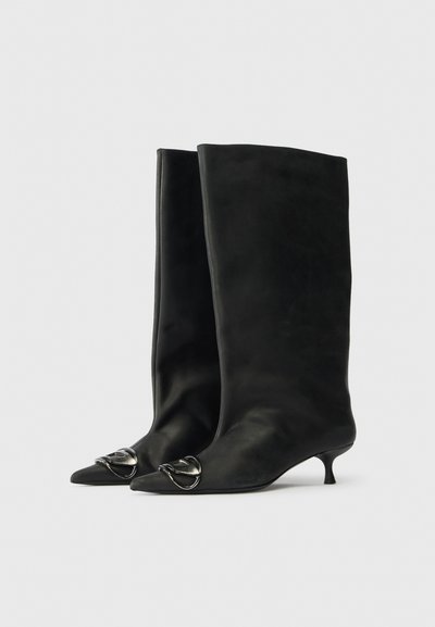 Bottes en cuir noir montant jusqu'au genou avec des pointes effilées, des talons kitten et des accents métalliques décoratifs près de la zone des orteils. Texture lisse.
