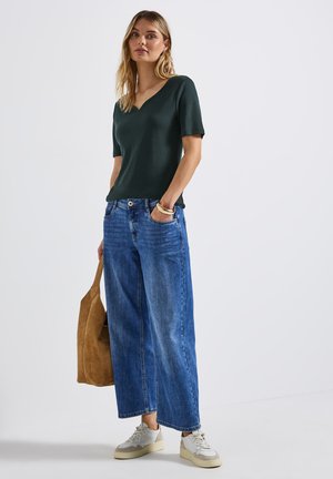 Maglietta verde scuro a maniche corte con scollatura a V abbinata a jeans denim blu a gamba larga. Accessoriata con una borsa beige e sneaker bianche.