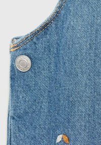 Denim stof in lichtblauw, met een afgeronde rand en contrasterende beige stiksel en een zilveren drukknoop. Kleine geborduurde details eronder.