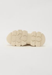 Beige rubber sneaker sole with deep treads, rectangular patterns, and a rounded front. Textured surface between treads for grip.