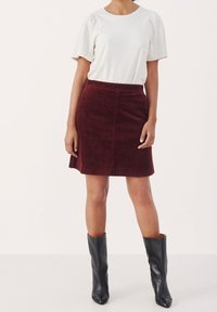 Top blanco de manga corta combinado con una falda de pana burdeos. La falda presenta una forma en A que favorece. La modelo lleva botas negras hasta la rodilla.