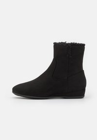 Bottes noires à la cheville en matériau semblable au daim, avec une doublure douce et texturée en fourrure en haut, un talon bas et des panneaux latéraux élastiques.